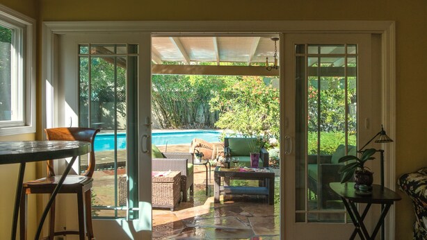 Ein Zimmer mit einer Schiebetür zu einer Terrasse mit Pool, Gartenmöbeln und einem Essbereich.