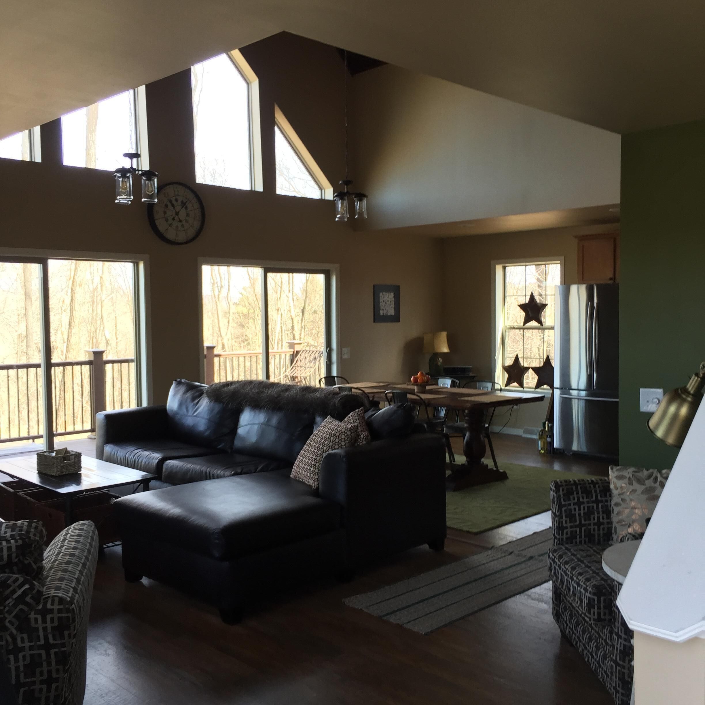 A spacious living room with a black leather sofa, a dining table, and a kitchen area with a refrigerator and star-shaped window decals.