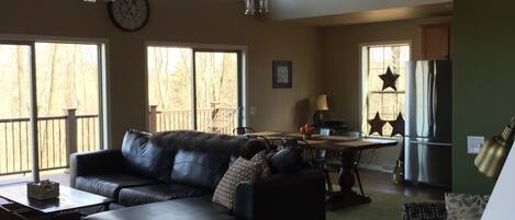 A spacious living room with a black leather sofa, a dining table, and a kitchen area with a refrigerator and star-shaped window decals.