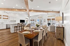 Une cuisine spacieuse avec des poutres en bois, des meubles blancs et un coin repas avec une table en bois, mise pour six personnes.