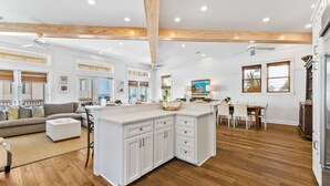 A spacious living area with a large island, wooden flooring, and a high ceiling with exposed beams. - Upscale Home with Breathtaking Gulf Views Steps to Beach + Pool w/7 Beach Bikes! (Inlet Beach)