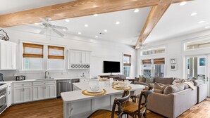 A spacious kitchen with white cabinets, a central island, and a dining area with a sofa and chairs. - Upscale Home with Breathtaking Gulf Views Steps to Beach + Pool w/7 Beach Bikes! (Inlet Beach)