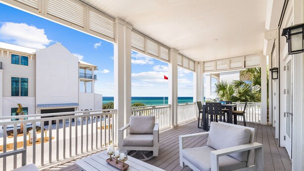 A covered outdoor area with white furniture, a table with candles, and a view of the ocean and buildings. - Upscale Home with Breathtaking Gulf Views Steps to Beach + Pool w/7 Beach Bikes! (Inlet Beach)