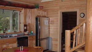 Interior de una cabaña de madera con cocina, comedor y escalera.