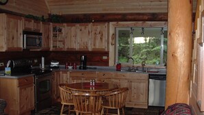 Interior acogedor de una cabaña con cocina de madera, comedor y ventana con vistas a la vegetación.