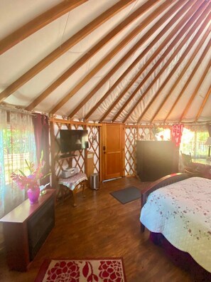 A tent with a wooden interior, a bed, a TV, and a desk with a computer.