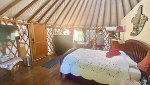 Un interior acogedor de una yurta con una cama, muebles de madera y un televisor.