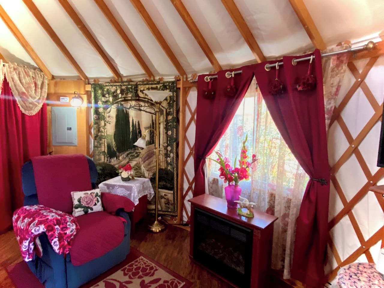 A cozy room with a wooden ceiling, a red chair, a small table with a vase, and a window with curtains.