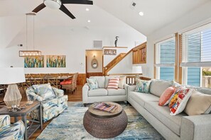 A spacious living room with a sofa, coffee table, and a dining area with chairs and a table. - Free Pool Heat on All New 2026 Reservations (Corolla)