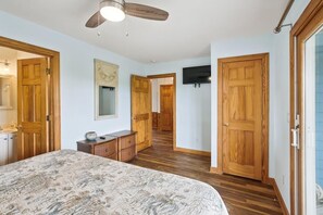 A bedroom with a bed, dresser, wooden doors, a ceiling fan, and a TV mounted on the wall.