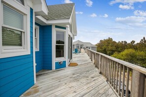 A wooden deck leading to a house with blue siding and a white door. - Free Pool Heat on All New 2026 Reservations (Corolla)