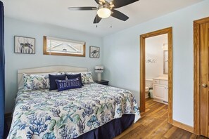 A bedroom with a bed, a ceiling fan, and a door leading to a bathroom. - Free Pool Heat on All New 2026 Reservations (Corolla)