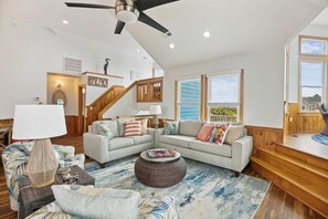 A spacious living room with a sectional sofa, a round coffee table, and a staircase leading to an upper level. - Free Pool Heat on All New 2026 Reservations (Corolla)