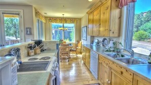 A kitchen with wooden cabinets, a dining area with a table and chairs, and a view of greenery outside. - Million Dollar Views! Walk to Restaurants, Shops, Trails. Hot tub, Lounges, Deck (Sedona)