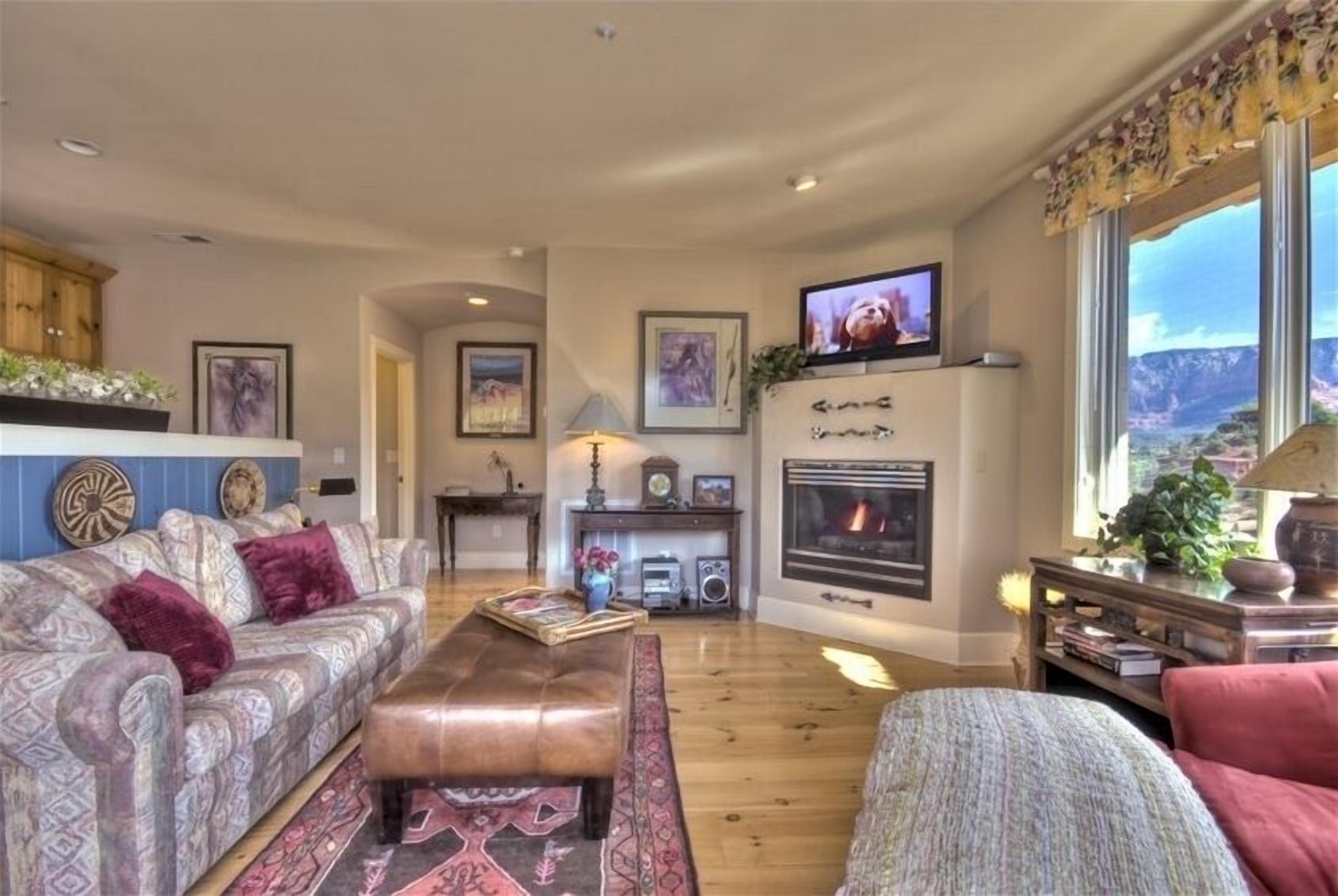 Sala de estar con sofá, reposapiés, chimenea, televisor y vista al exterior.