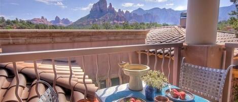 Un balcón con una mesa para dos, un jarrón con flores y vistas a formaciones rocosas rojas.