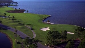 Un campo de golf costero con un obstáculo acuático, búnkeres de arena y vista despejada del océano.
