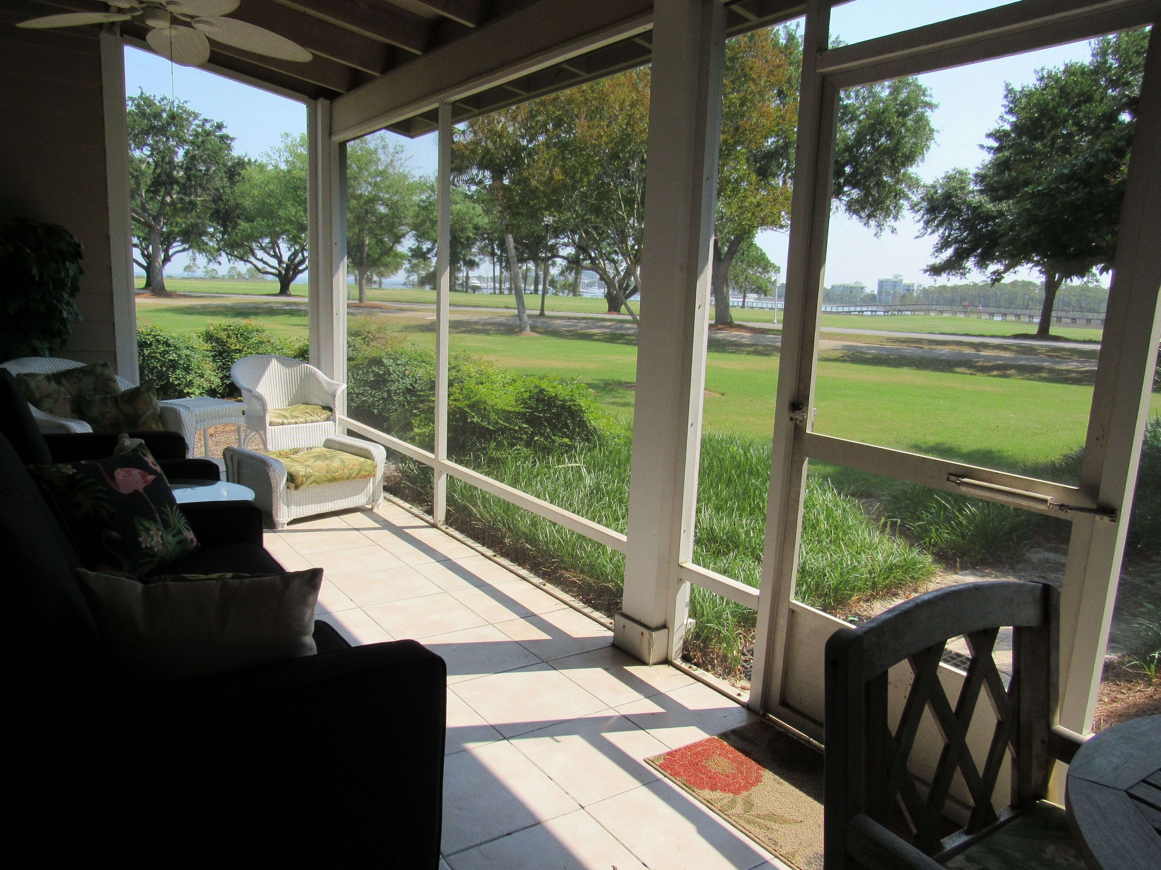 A covered porch with wicker furniture and a view of a park.