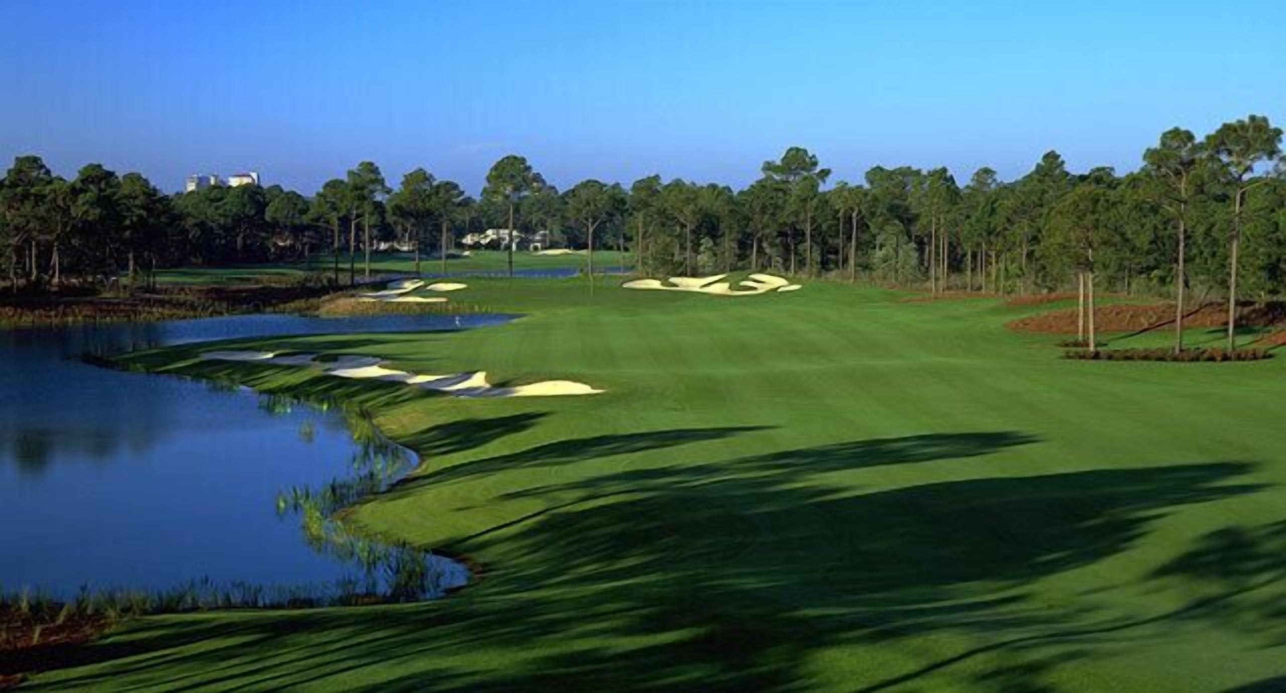A golf course with a pond, sand bunkers, and a clear sky.