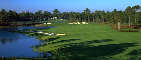 A golf course with a pond, sand bunkers, and a clear sky.