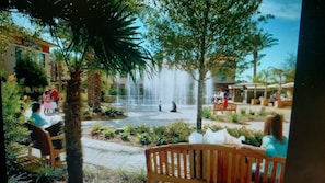 Relax in a serene oasis surrounded by lush greenery and palm trees, with a soothing fountain and comfortable benches.