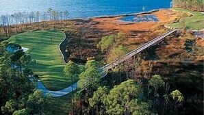 Campo de golf con un obstáculo acuático, un puente y vista al océano.