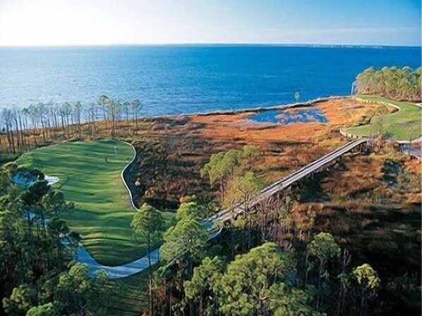 Un campo da golf con un ostacolo d'acqua, un ponte e vista sull'oceano.