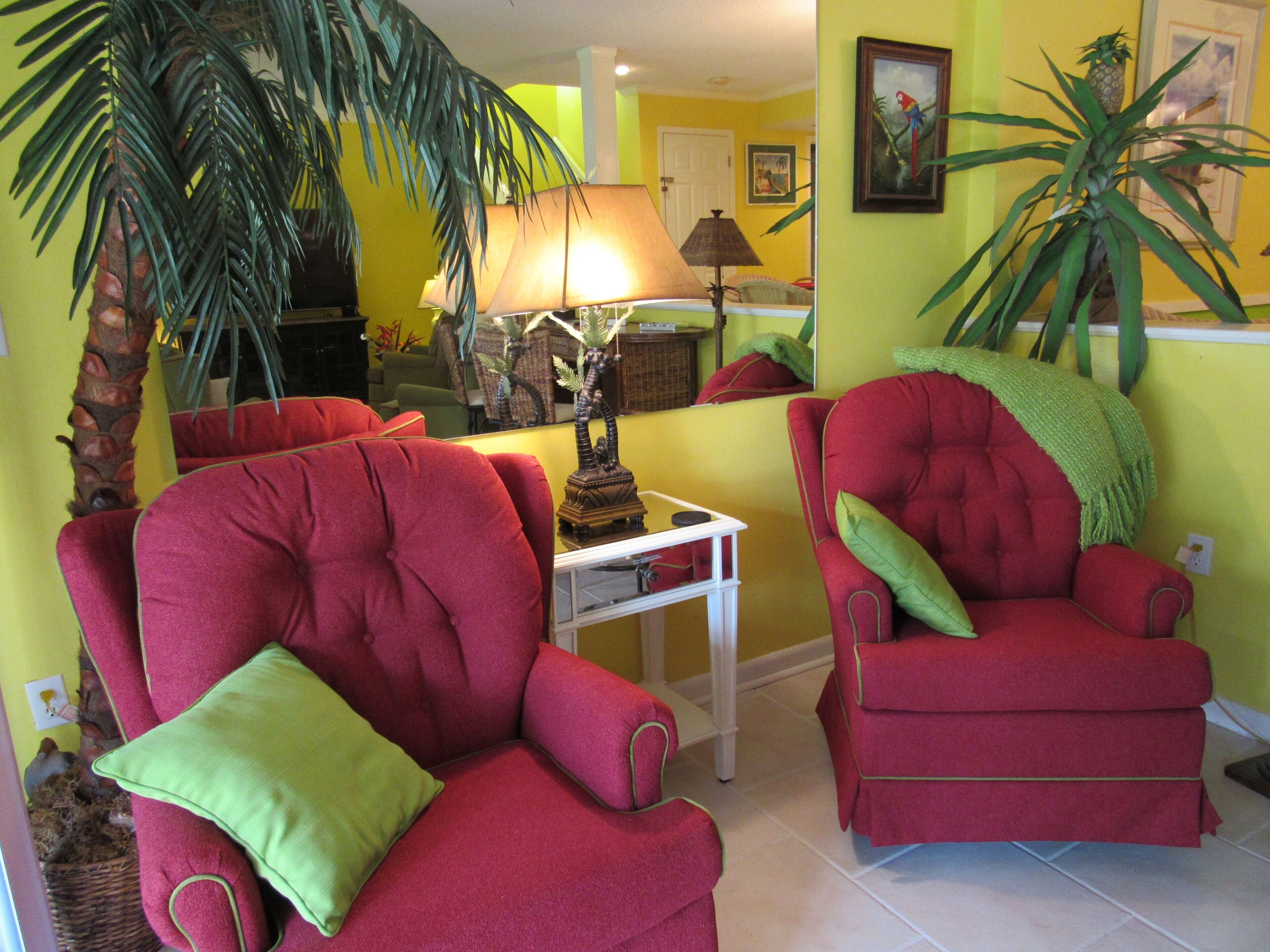 A living room with red armchairs, a lamp, a small table, and a potted plant.