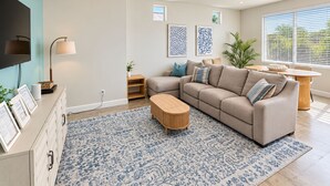 Ein modernes Wohnzimmer mit einer Eckcouch, einem Couchtisch, einem Fernseher und Kunstwerken an den Wänden.