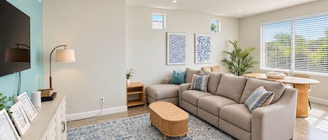 A modern living room with a sectional sofa, a coffee table, a TV, and artwork on the walls.