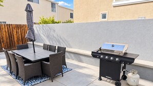 Eine Außenpatio mit Grill, Esstisch, Stühlen und einem Holzzaun.