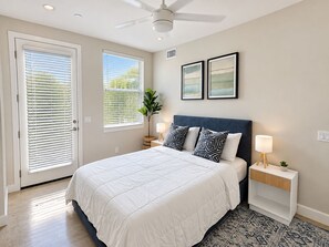 A bedroom with a bed, bedside tables, a ceiling fan, and two windows with blinds.
