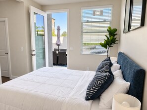 A bedroom with a bed, a nightstand, a potted plant, and a window with blinds.