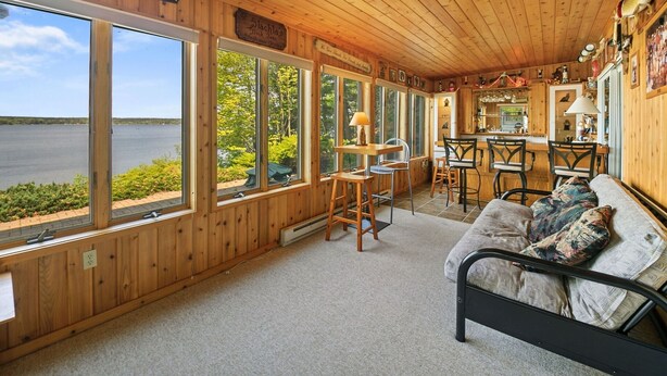 A cozy cabin with a large window overlooking a lake, a dining area with wooden chairs, and a bed with a patterned blanket. - Executive Lake Home on Premier Lake w Game Room & Sauna–Ultimate Retreat Awaits! (Webster)