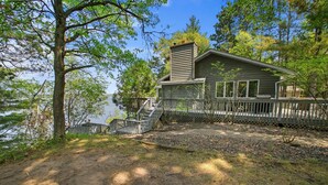 A cabin with a deck, a chimney, and a view of the lake. - Executive Lake Home on Premier Lake w Game Room & Sauna–Ultimate Retreat Awaits! (Webster)