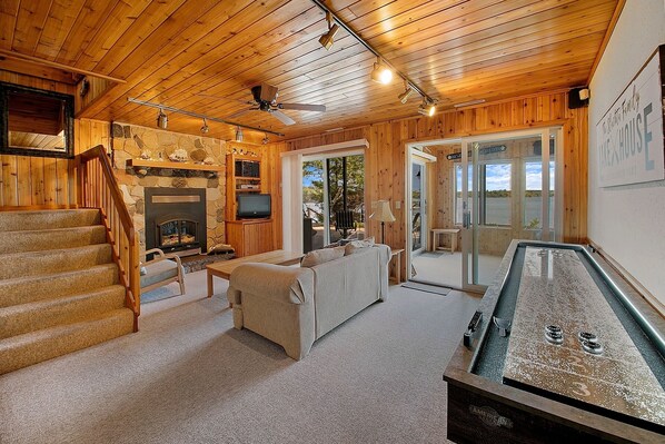 A cozy cabin interior with a stone fireplace, wooden floors, a sofa, and a pool table.