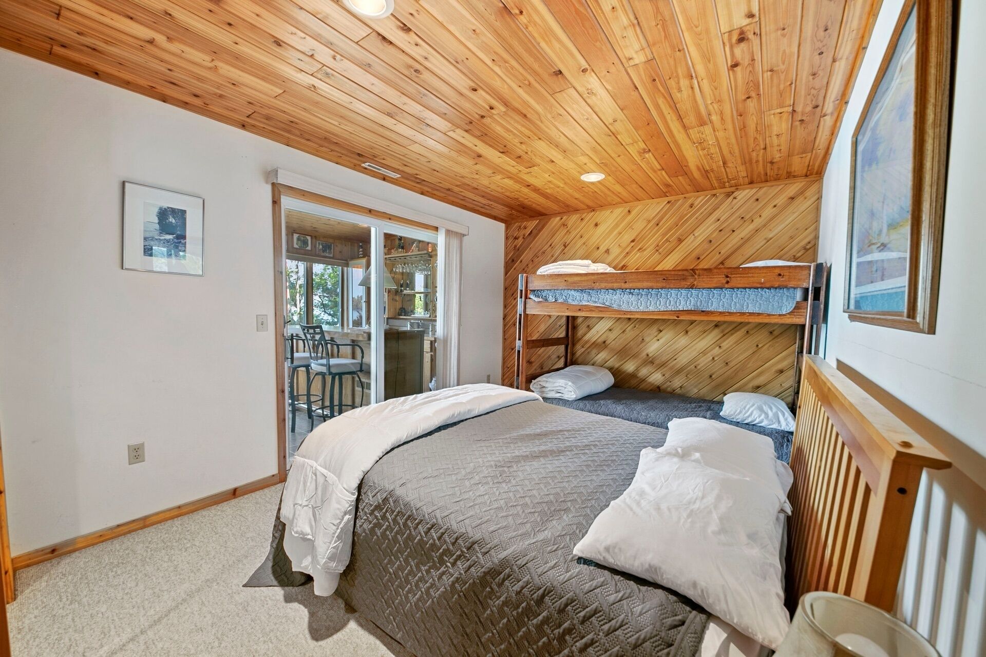A room with a bunk bed, a large bed, and a dining area with chairs and a table.