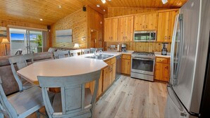 A cabin interior with a wooden interior, a dining area, kitchen with appliances, and a view through the window. - Executive Lake Home on Premier Lake w Game Room & Sauna–Ultimate Retreat Awaits! (Webster)