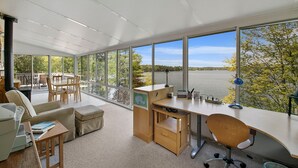 A modern office with large windows overlooking a lake, a desk with a computer, and a comfortable seating area. - Executive Lake Home on Premier Lake w Game Room & Sauna–Ultimate Retreat Awaits! (Webster)