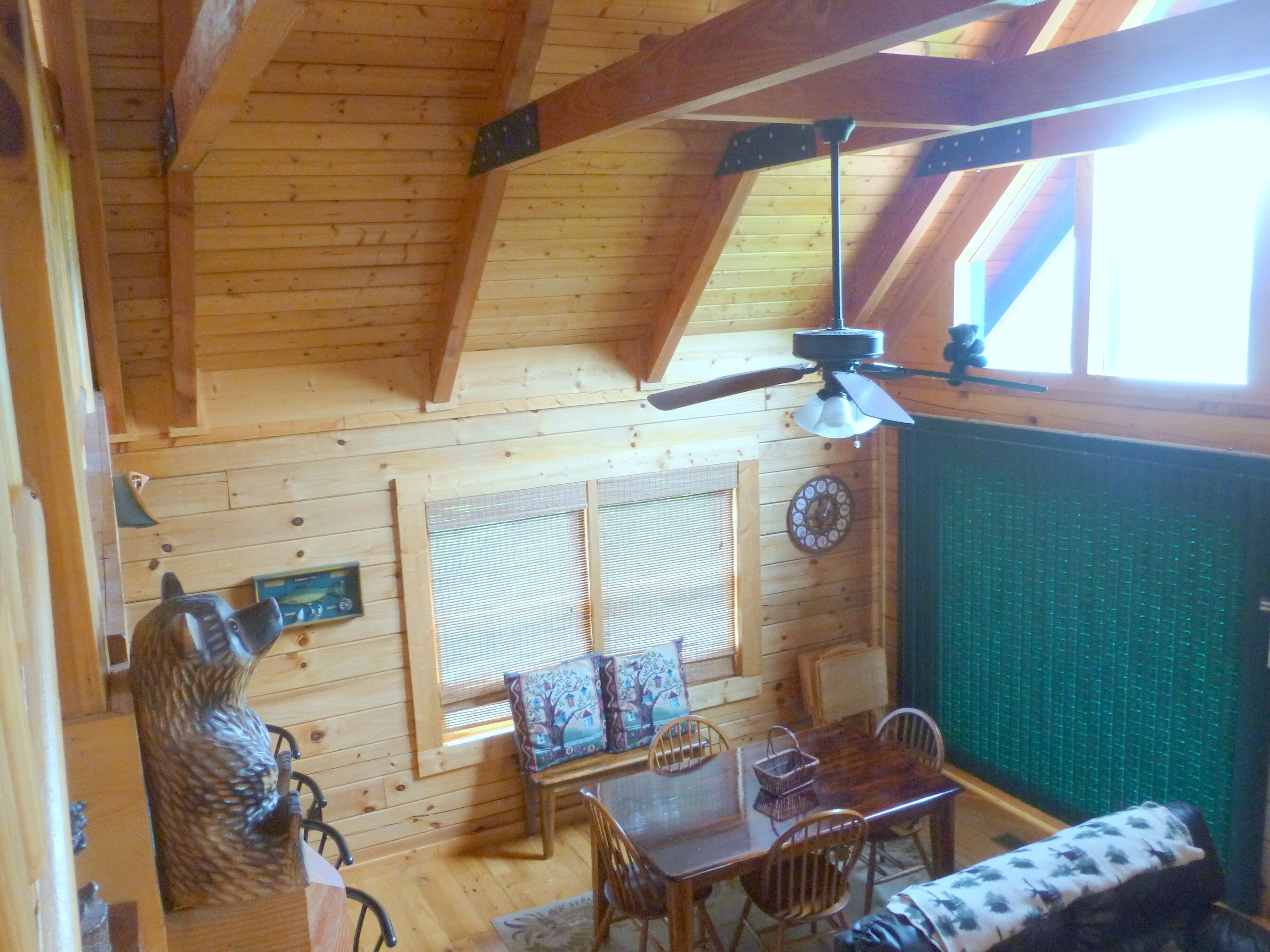 A wooden interior with a dining area, a ceiling fan, a clock, and a window with blinds.