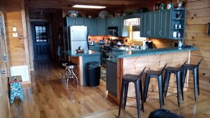 Interieur van een houten chalet met een keukenhoek, inclusief een centraal eiland, barkrukken en een koelkast.