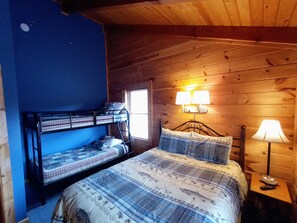Habitación con literas, pared azul, techo de madera, dos lámparas de noche y una mesita de noche con un control remoto.
