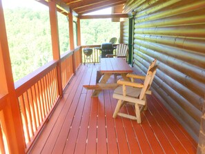 Una terraza de madera con una mesa de picnic y sillas, una parrilla de barbacoa y vistas al bosque.