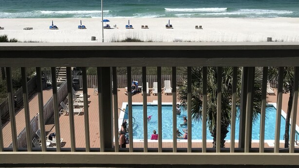 A beach view from a balcony with a pool area, including lounge chairs and umbrellas. - Updated, spacious Gulf-front Condo- just steps to the beach! (Panama City Beach)