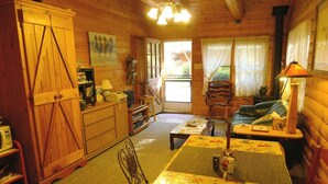 Ein gemütliches Blockhaus-Interieur mit Esstisch, Stühlen, einer Couch, einem Kamin und einer Küchenzeile.
