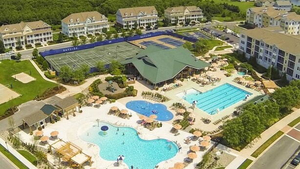 A resort with multiple swimming pools, tennis courts, and a large building with a green roof. - SUPER 5 BR, 3.5 bath, sleeps 12, heart of Bayside! EV charger (Selbyville)