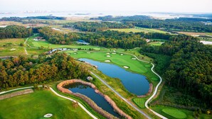 An aerial view of a golf course with multiple greens, water hazards, and a large pond. - SUPER 5 BR, 3.5 bath, sleeps 12, heart of Bayside! EV charger (Selbyville)