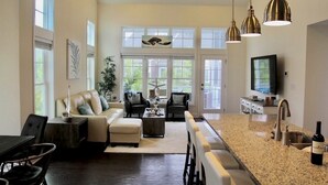 A spacious living room with a large window, a dining area, and a kitchen with granite countertops and a sink. - SUPER 5 BR, 3.5 bath, sleeps 12, heart of Bayside! EV charger (Selbyville)
