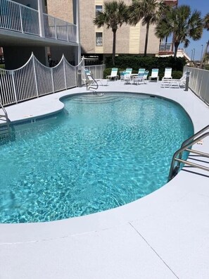 A clear, curved pool with a metal ladder and lounge chairs around it. - Direct Beach Front Tropic Isles 604 (Gulf Shores)