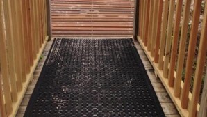 Una passerella in legno conduce a una spiaggia, delimitata da ringhiere in legno e da un tappetino nero all'ingresso.
